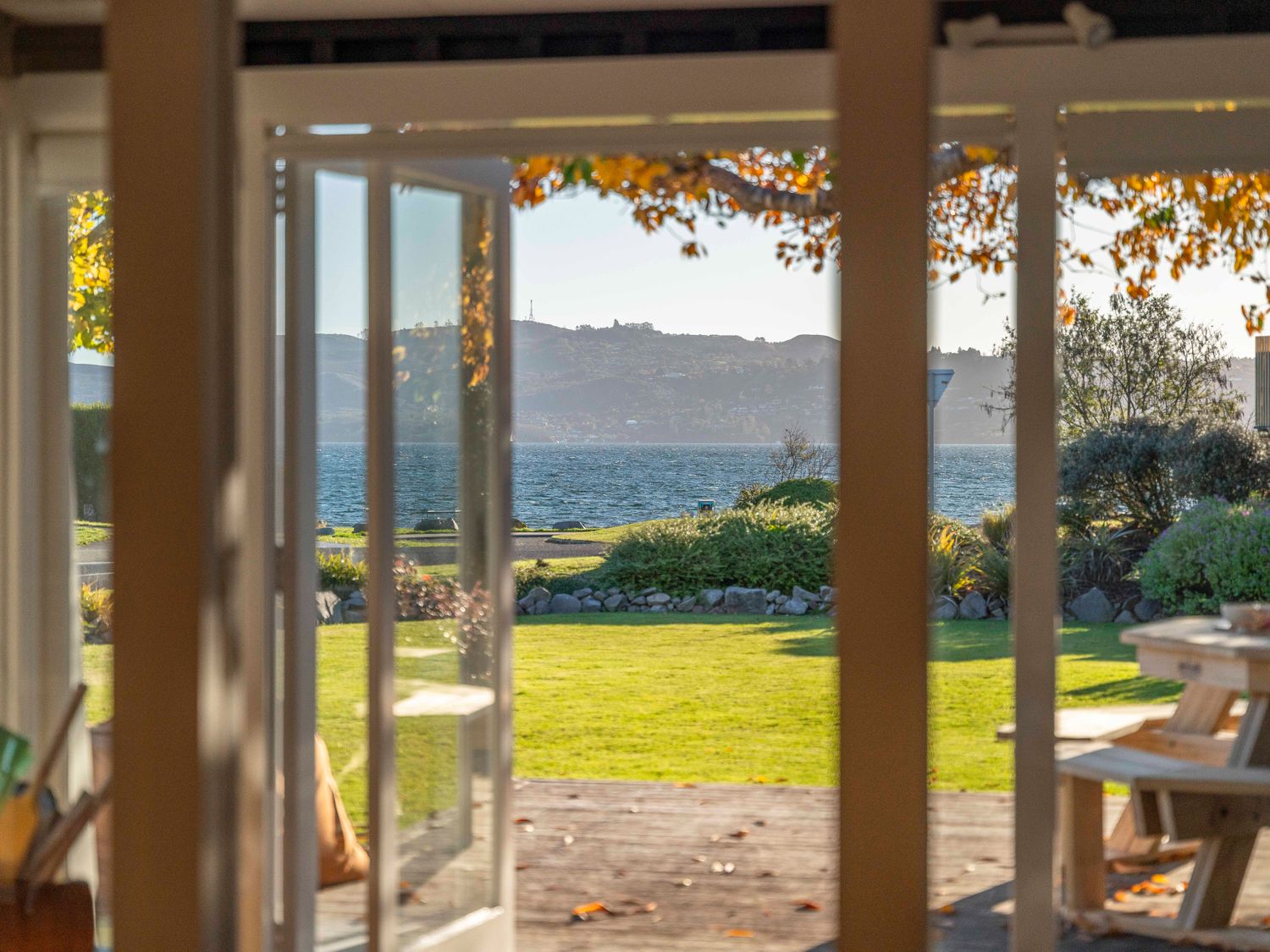A view through open doors onto a lawn and lake with hills in the background at Waterside Bliss Taupo Central