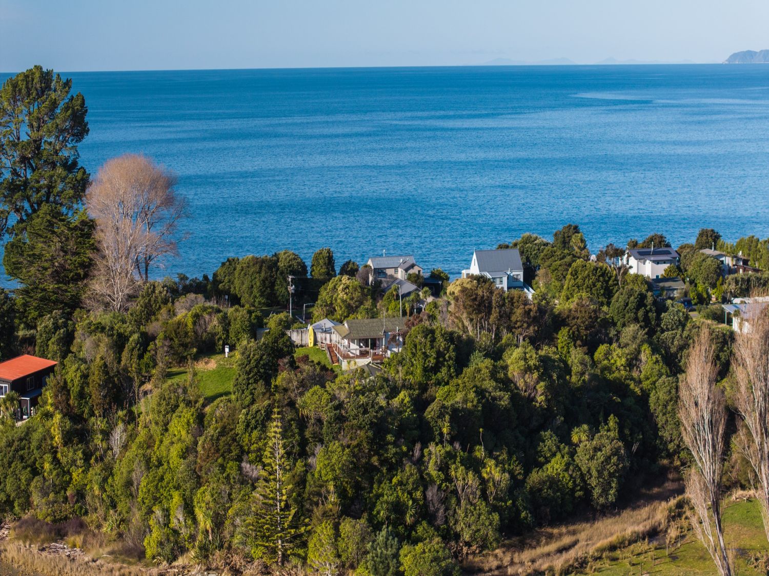 A view of houses and trees near the ocean at Quail Rise - Collingwood Holiday Home Parapara Beach