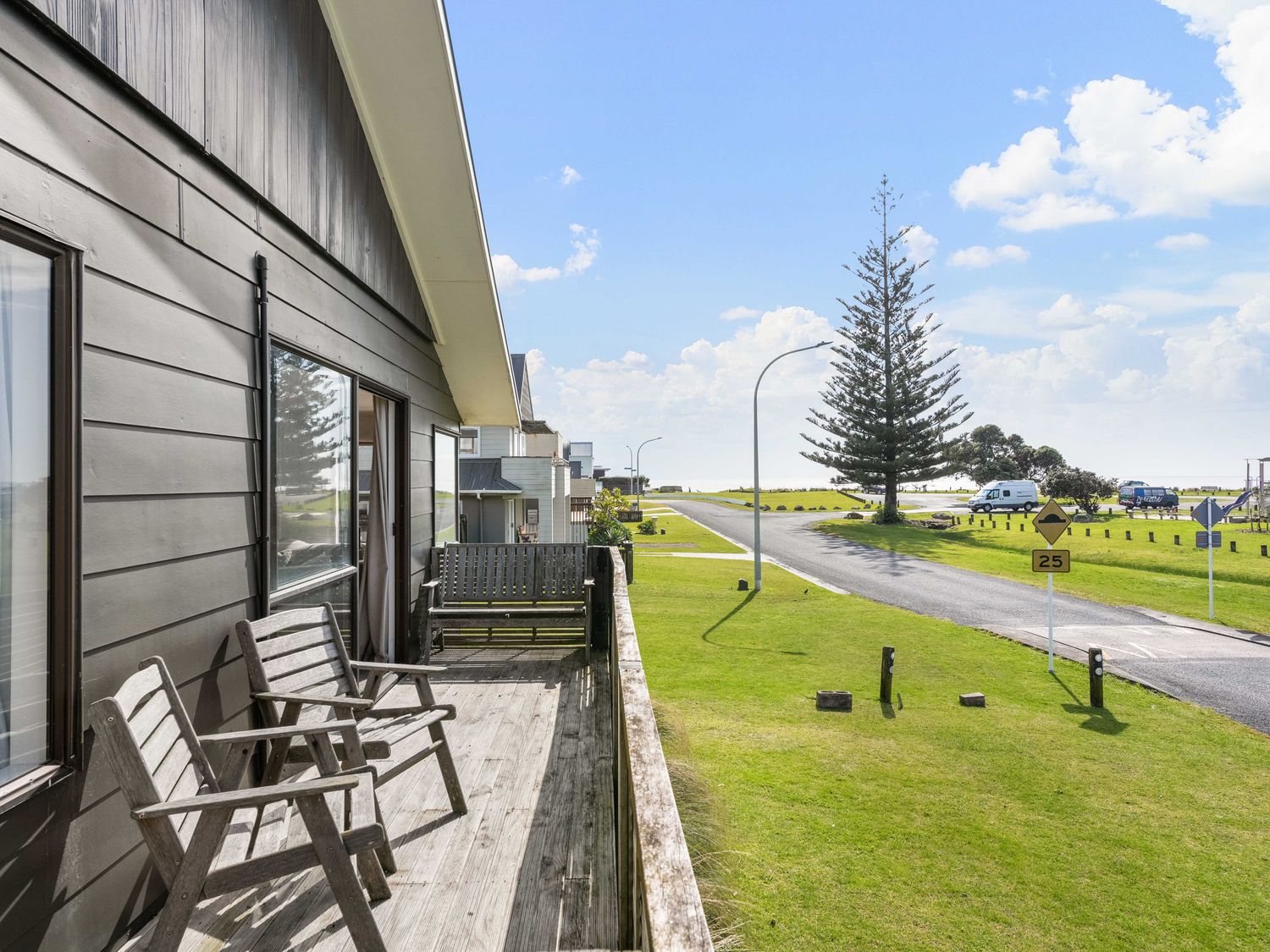 An outdoor patio with chairs overlooking a road at Waihi Beach Holiday Home in Waihi Beach