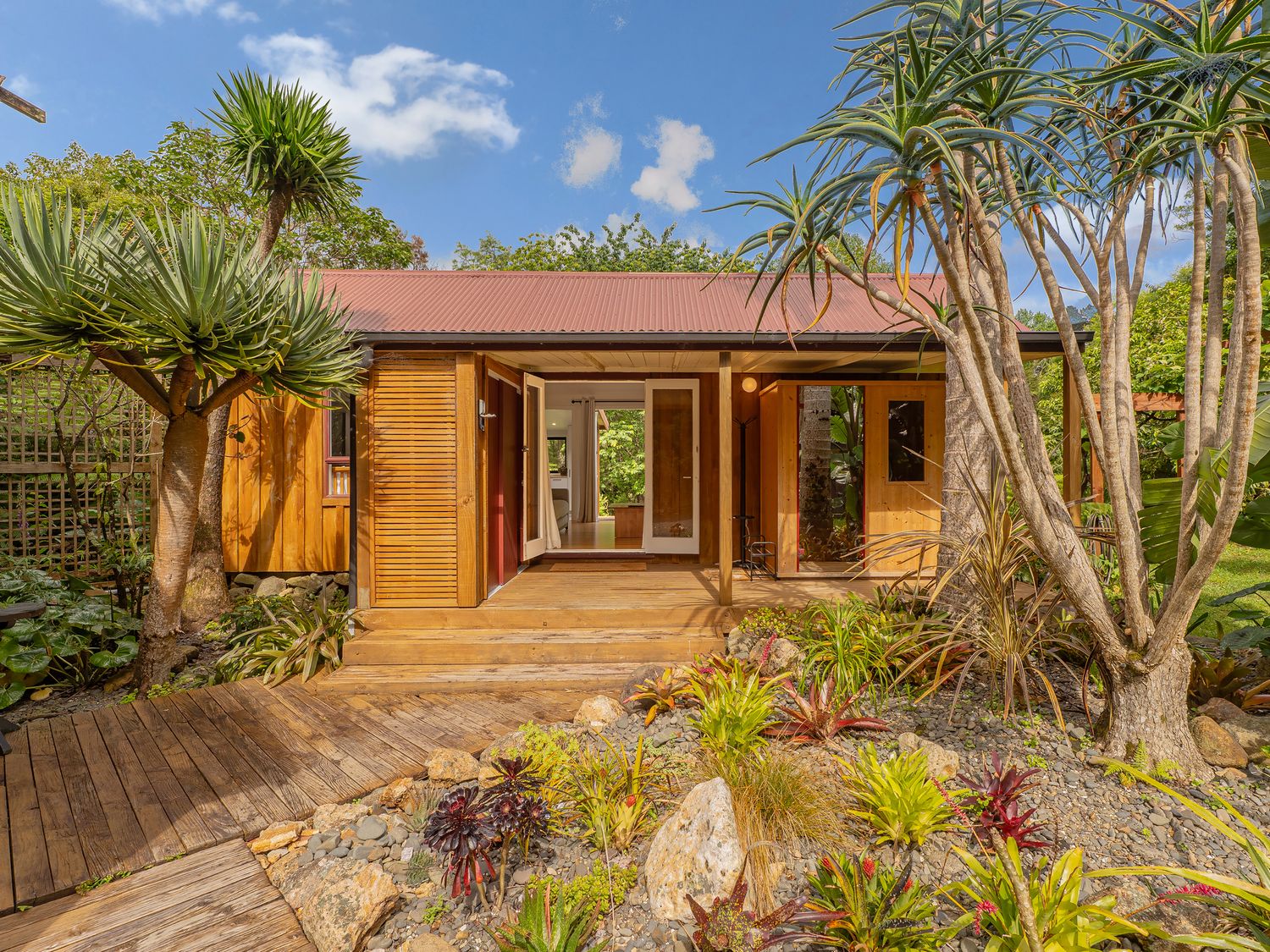 A house with plants and a wooden deck at Stream-side Cottage - Driving Creek Coromandel