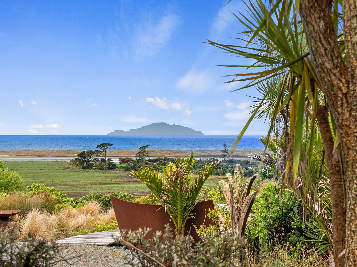 A garden view with plants and ocean at Black Dune in Waipu