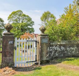 A white wooden gate between stone pillars opening to a garden with trees at Fenwick Retreat at Fenwick Lodge in Fenwick near Ponteland