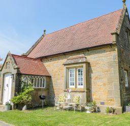 A stone cottage with a tiled roof outdoor chairs and table with flowers and grill at Fenwick Retreat at Fenwick Lodge Fenwick near Ponteland