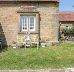 A garden with white metal chairs and a table with flowers against a stone house wall at Fenwick Retreat at Fenwick near Ponteland