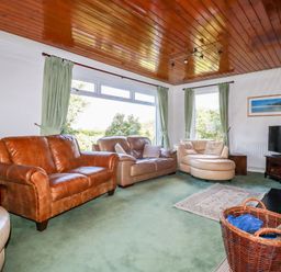 A living room with leather sofas a television on a stand and a basket with firewood at Trevow in Camborne
