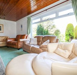 A living room with multiple leather sofas green curtains and large window at Trevow Camborne