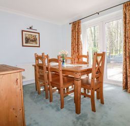 A dining room with wooden table and chairs and floral curtains at Trevow in Camborne