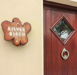 A wooden door with a diamond-shaped glass window and a metal knocker beside a wooden sign reading Silver Birch at Silver Birch in Dromelihy Cooraclare County Clare