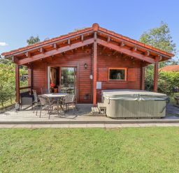 A wooden cabin with a covered porch featuring a table with chairs and a hot tub in a grassy yard at Jemima Lodge in Tattershall