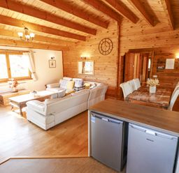 A living area with a white sectional sofa wooden tables a dining table with chairs and wooden walls at Jemima Lodge in Tattershall