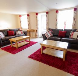 A living room with two brown leather sofas red cushions wooden coffee tables and patterned curtains at Tyn Y Buarth in Dyffryn Ardudwy