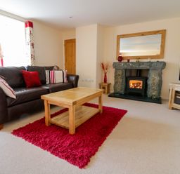 A living room with a brown leather sofa red rug wooden coffee table stone fireplace and television at Tyn Y Buarth in Dyffryn Ardudwy
