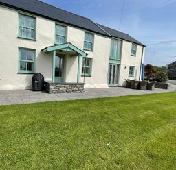 The exterior of a two story house with green framed windows a door and patio furniture on the side at Tyn Y Buarth in Dyffryn Ardudwy