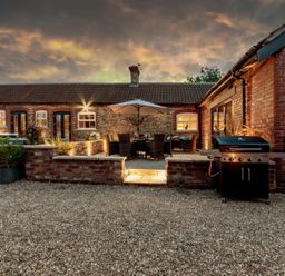 An outdoor patio with a dining table under an umbrella a grill and brick walls at Sykes Lodge in Malton