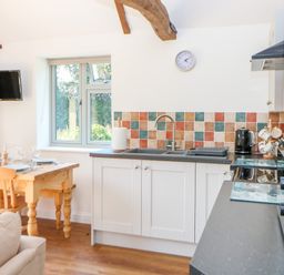 A kitchen and dining area with a wooden table set for four and white cabinets with a tiled backsplash at Sparrow Barn in Reepham