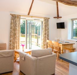 A living room with beige sofas and wooden dining table near open doors at Sparrow Barn in Reepham