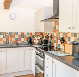 A kitchen with white cabinets a black countertop a stove a microwave a kettle and colorful tiled backsplash at Sparrow Barn in Reepham