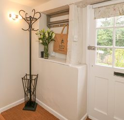 An entrance hall with a coat stand a vase of flowers a wall hook shelf a tote bag and a white door with glass panes at Rookwood in Drewsteignton
