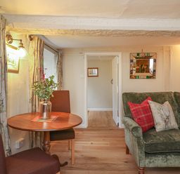 A room with a round wooden table and two brown chairs next to a green sofa with cushions and an open doorway at Rookwood in Drewsteignton