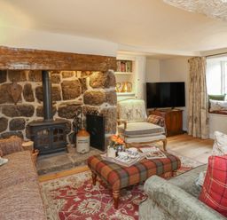 A living room with a stone fireplace wood stove plaid ottoman sofas and armchair at Rookwood in Drewsteignton
