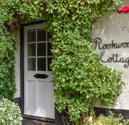 A white wooden door surrounded by green vines with a sign reading Rookwood Cottage on the wall at Rookwood in Drewsteignton
