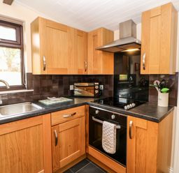 A kitchen with wooden cabinets a black countertop a stainless steel sink an oven and a microwave at Daffodil Lodge Saltburn-by-the-Sea