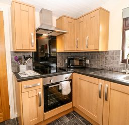 A kitchen with wooden cabinets black countertop microwave oven stove and a window at Foxglove Lodge in Saltburn-By-The-Sea