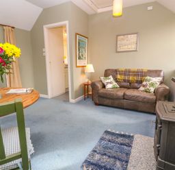 A living room with a brown leather sofa and a wood stove at Higher Lampra in Mullion