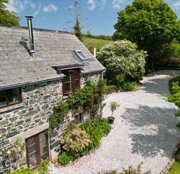 A stone house with a slate roof next to a gravel driveway and surrounded by trees and bushes at Higher Lampra in Mullion