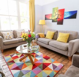 A living room with two sofas a colorful rug a round glass coffee table with flowers and a lamp on a stand at The Cottage at Broadway in Broadway