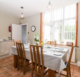 A dining table set with plates glasses and cutlery in a kitchen with a large window and wooden chairs at The Cottage at Broadway in Broadway