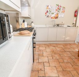 A kitchen with a microwave oven bread on cutting board stove and sink with cabinets and a dining table with chairs at The Cottage at Broadway in Broadway
