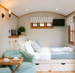 A small bedroom with a bed a turquoise armchair a wooden tray with cups and a wall-mounted television at Little Silver Leaf in High Bickington