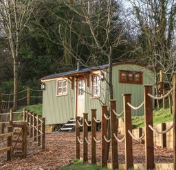 A small green corrugated metal cabin with wooden trim in a fenced outdoor area with trees at Little Silver Leaf in High Bickington