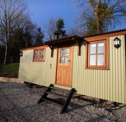 A small green corrugated metal cabin with wooden framed windows and door on gravel at Little Silver Leaf in High Bickington