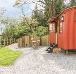 An outdoor area with a red metal cabin a wooden table and chairs and a wooden fence at Little Silver Owl in High Bickington