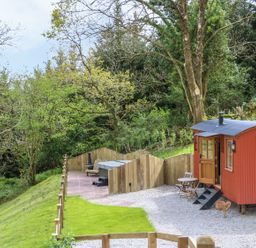 A red shepherds hut with steps and outdoor seating near a fenced grassy area at Little Silver Owl in High Bickington