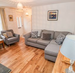 A living room with gray sofas wooden floor wooden side table and a lamp at Coeden Bach in Burry Port
