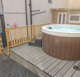 A hot tub on a wooden deck with a black door and wooden fence in the background at Coeden Bach in Burry Port