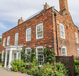 A brick house with white windows and columns with flowers and plants around at The Manor House in Scarborough