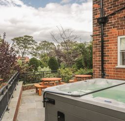 An outdoor patio area with a hot tub two wooden picnic tables and surrounding greenery at The Manor House in Scarborough