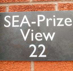 A black sign with white text reading SEA-Prize View 22 mounted on a red brick wall at Sea-Prize View in Old Colwyn