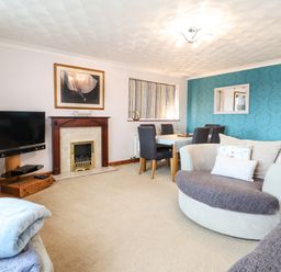 A living room with a fireplace dining table chairs and curved sofa at Sea-Prize View in Old Colwyn