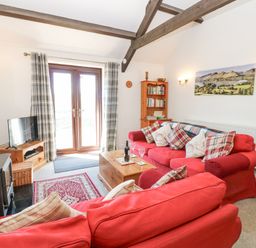 A living room with red sofas a wooden coffee table a television and French doors at Dale View Cottage in Allendale near Hexham