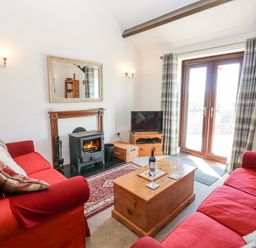 A living room with two red sofas a wooden coffee table a wood burning stove and glass doors with plaid curtains at Dale View Cottage in Allendale near Hexham