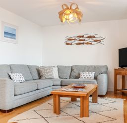 A living room with a gray sectional sofa wooden coffee table and television at Ocean Blue in Praa Sands