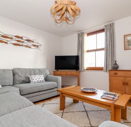 A living room with a gray sofa wooden coffee table wooden sideboard and TV at Ocean Blue in Praa Sands