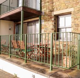 An outdoor patio area with wooden chairs and tables behind a green metal railing at Ocean Blue in Praa Sands