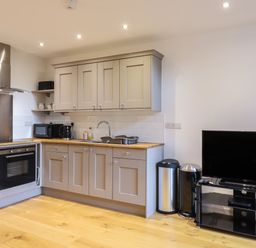 A kitchen with grey cabinets microwave kettle oven and a television on a stand at Grange Barn in Gedding near Felsham