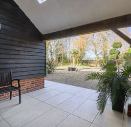 A covered patio area with a black bench and potted plant overlooking a gravel garden at Grange Barn in Gedding near Felsham